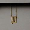 Gold necklace with a geometric pendant on a gray background