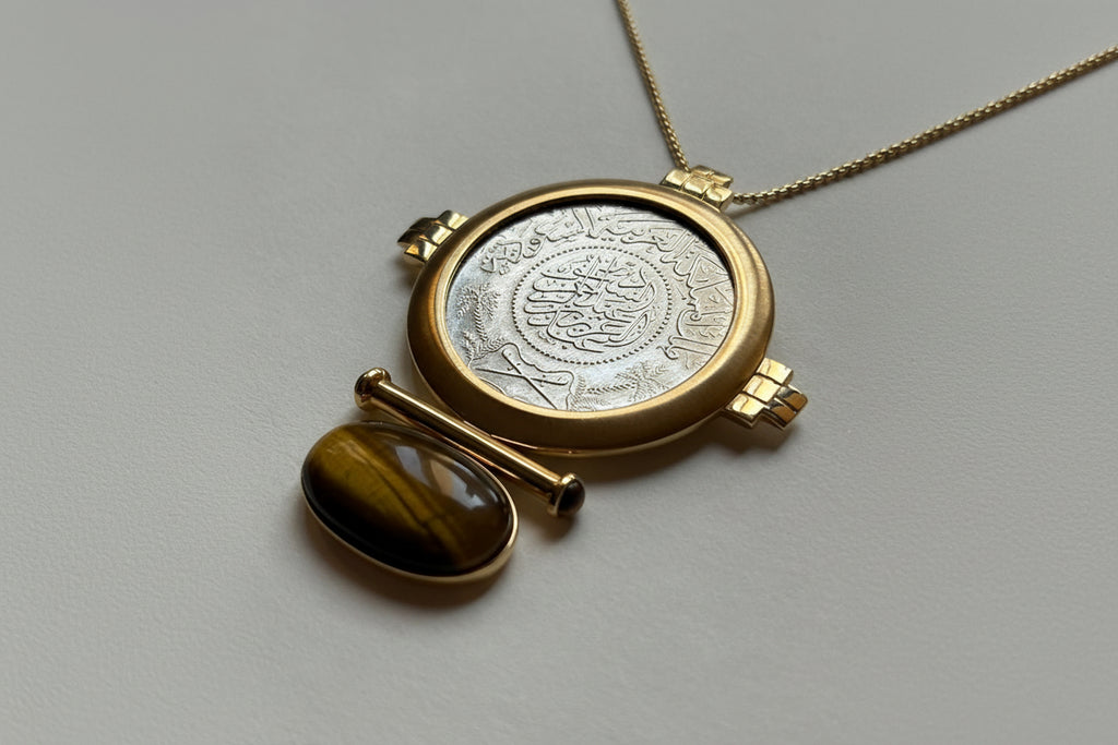 Gold pendant with a silver coin insert on a gray background