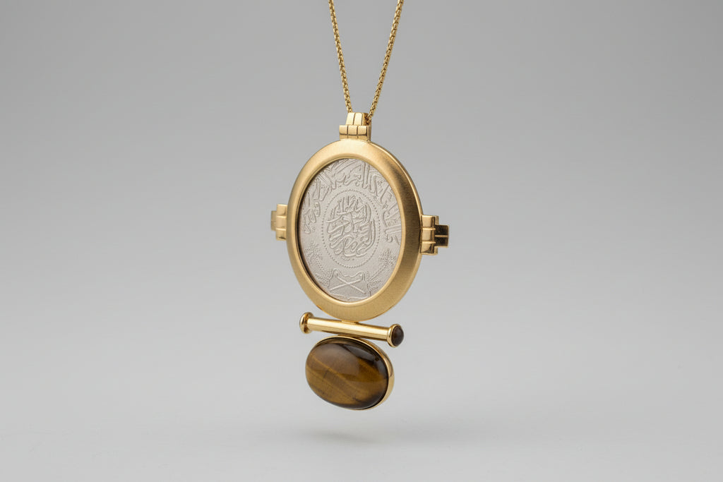 Gold locket with engraved design and tiger's eye stone on a light gray background