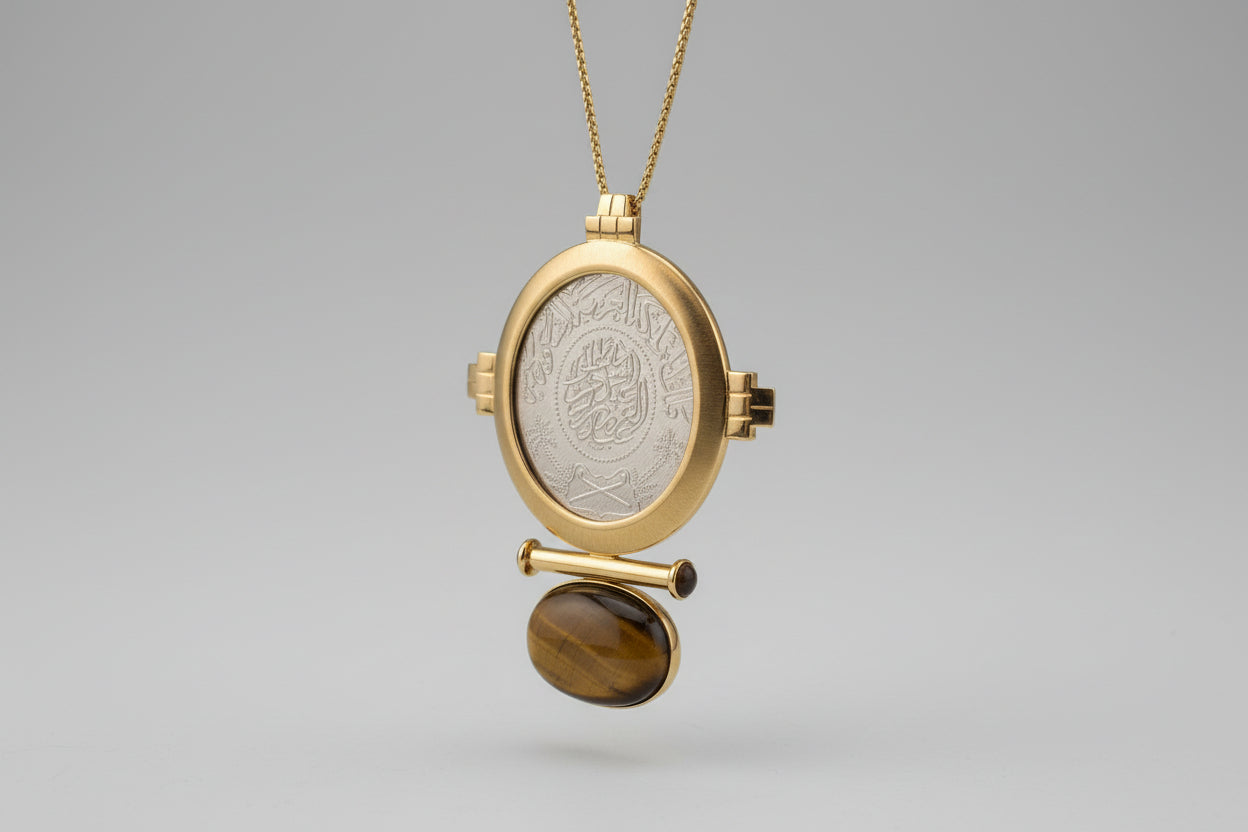 Gold locket with engraved design and tiger's eye stone on a light gray background