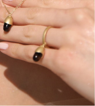 Gold necklace with black beads held by a hand against a neutral background