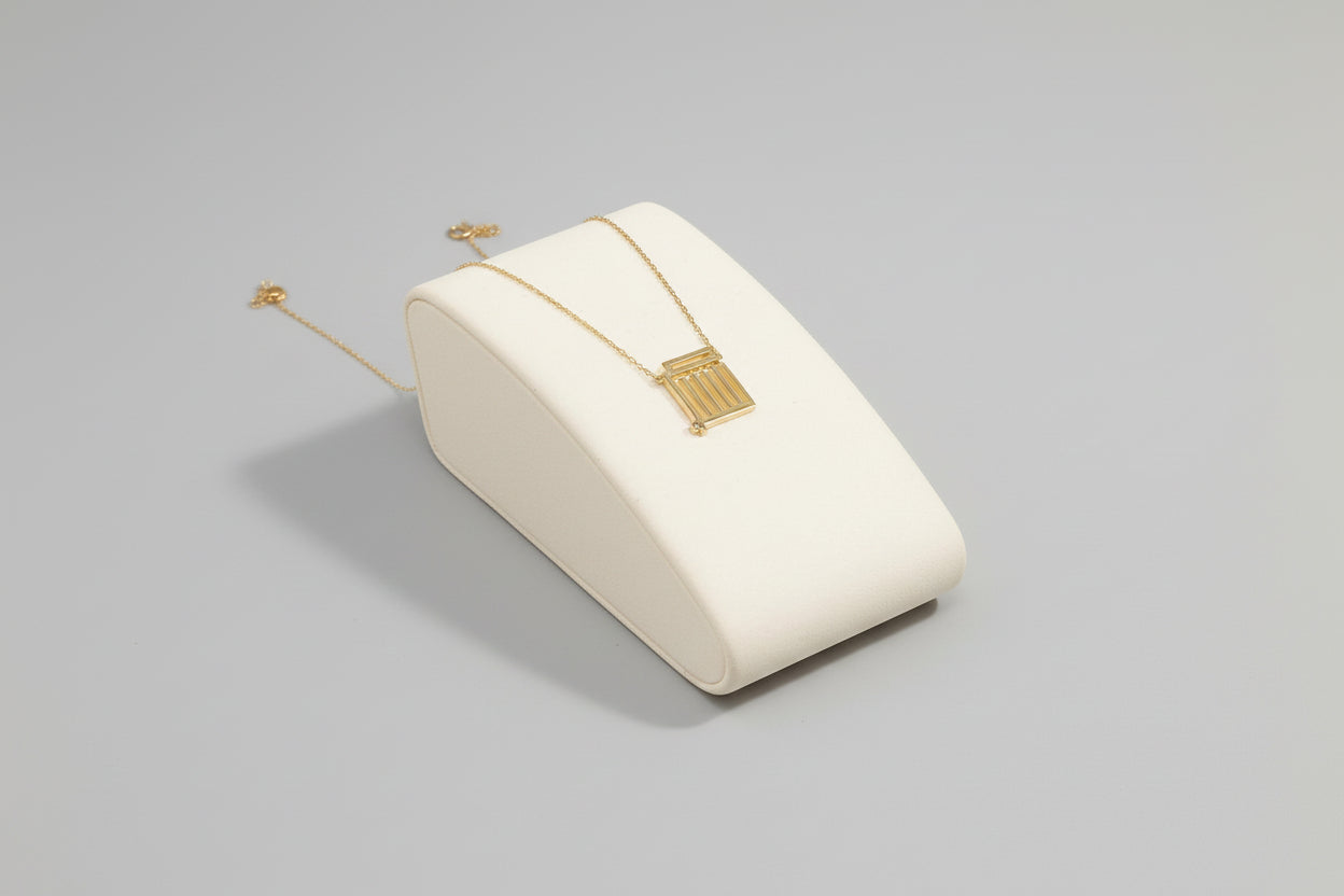 A gold necklace with a geometric pendant displayed on a white surface.