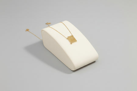 A gold necklace with a geometric pendant displayed on a white surface.