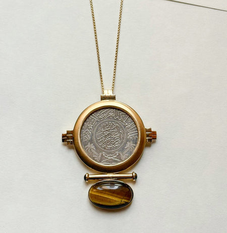 Gold pendant necklace with a circular design and tiger's eye stone on a white background